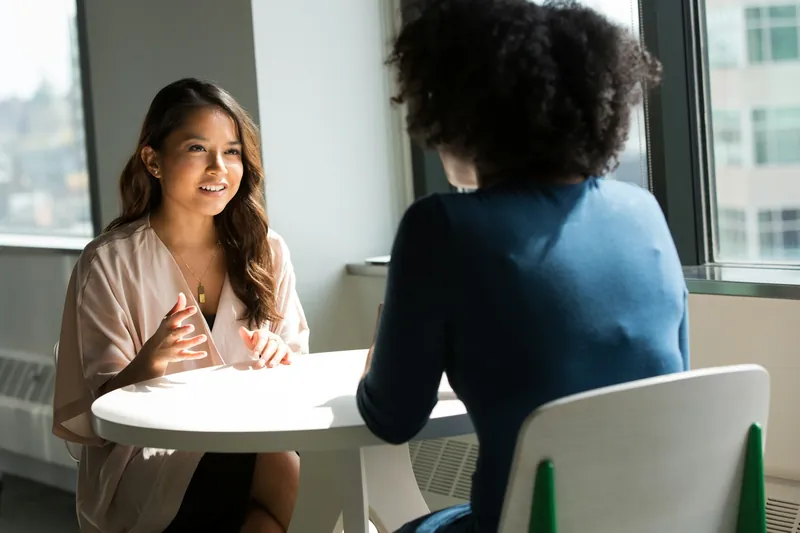 Two women talking across a small white table during a coaching session