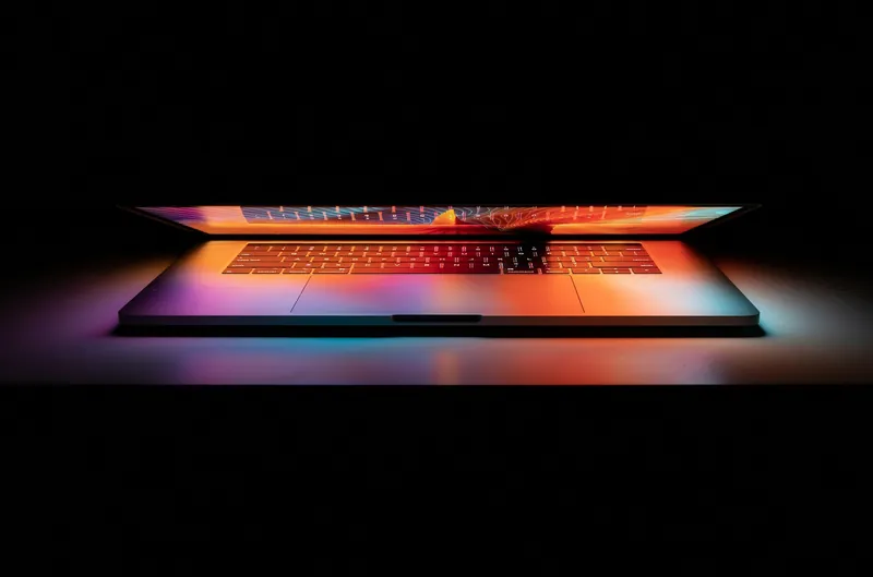 Half-open laptop glowing with orange and blue light in a dark room