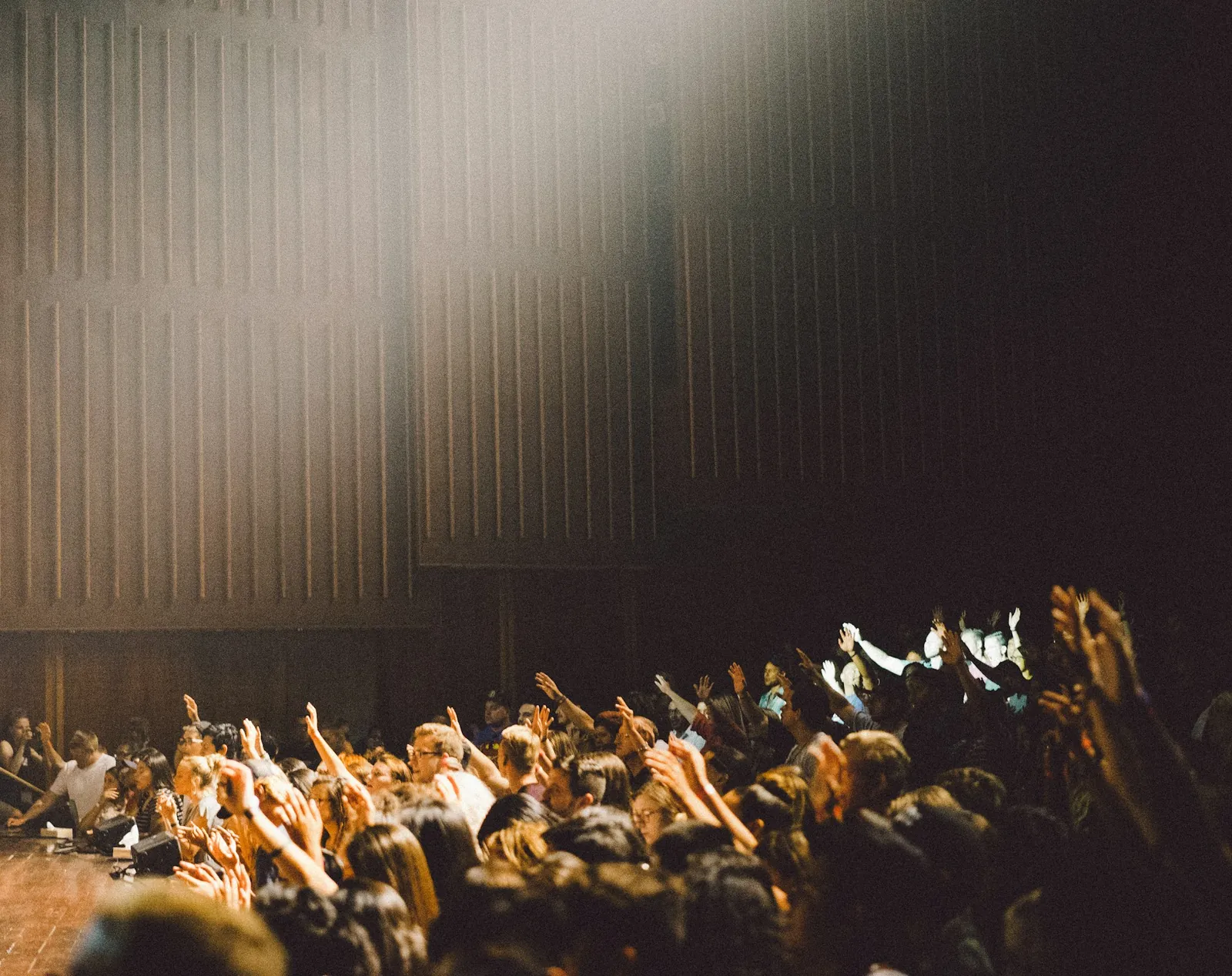 Crowd of students raising their hands in a large hall lit by a spotlight