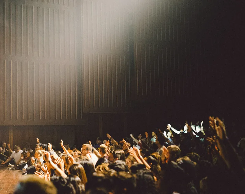 Crowd of students raising their hands in a large hall lit by a spotlight