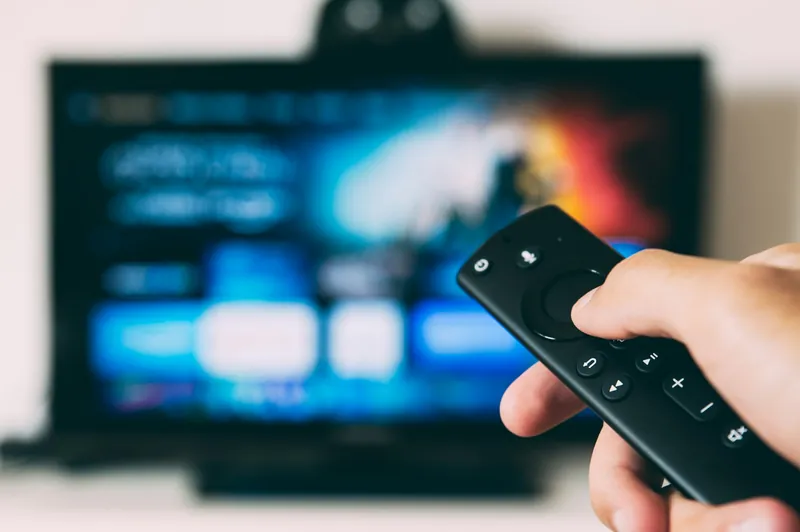 Hand holding a streaming remote control in front of a television screen