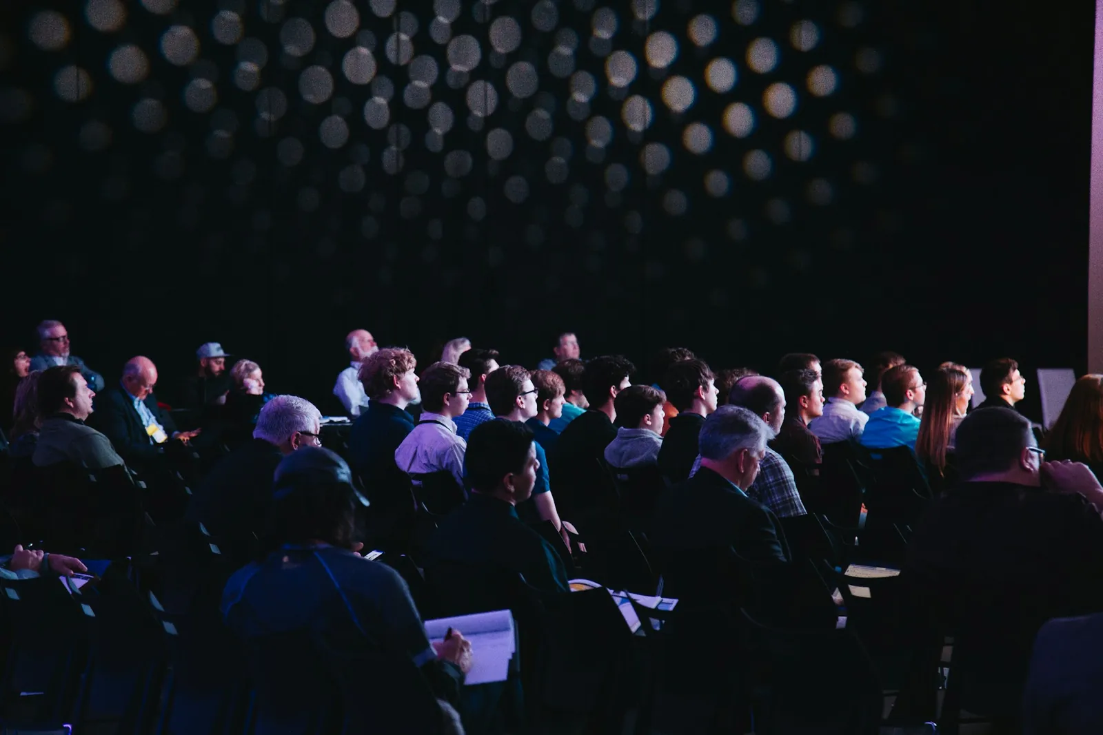 Audience seated in a dark conference hall watching a talk