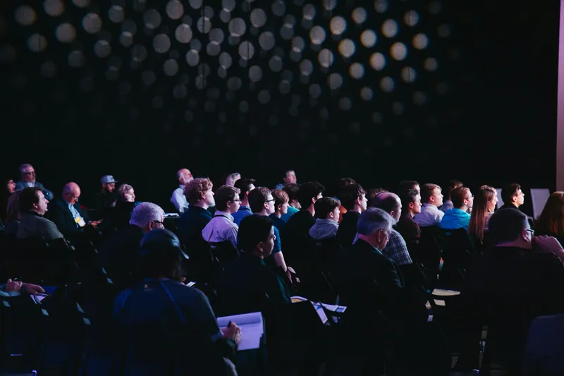 Audience seated in a dark conference hall watching a talk