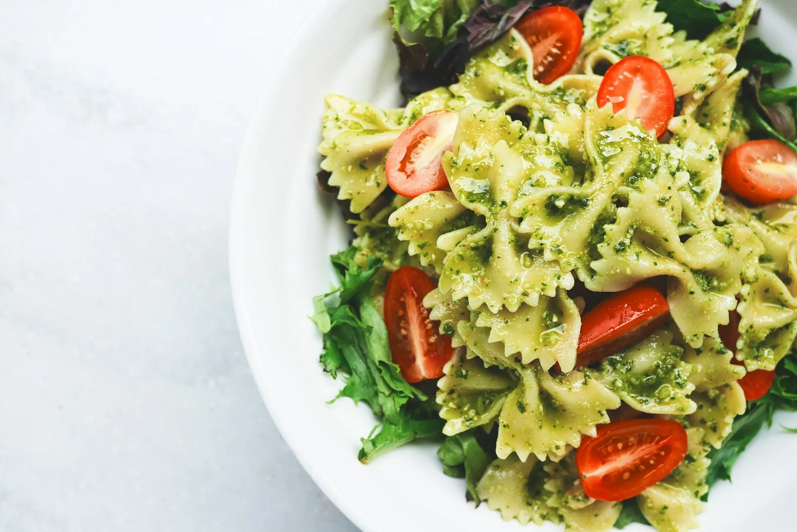 Bowl of farfalle pasta with pesto, cherry tomatoes and salad leaves