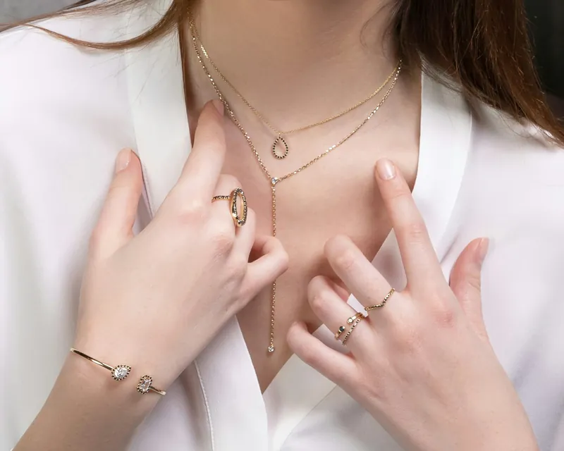 Close-up of delicate gold necklaces, rings and a bracelet worn with a white shirt