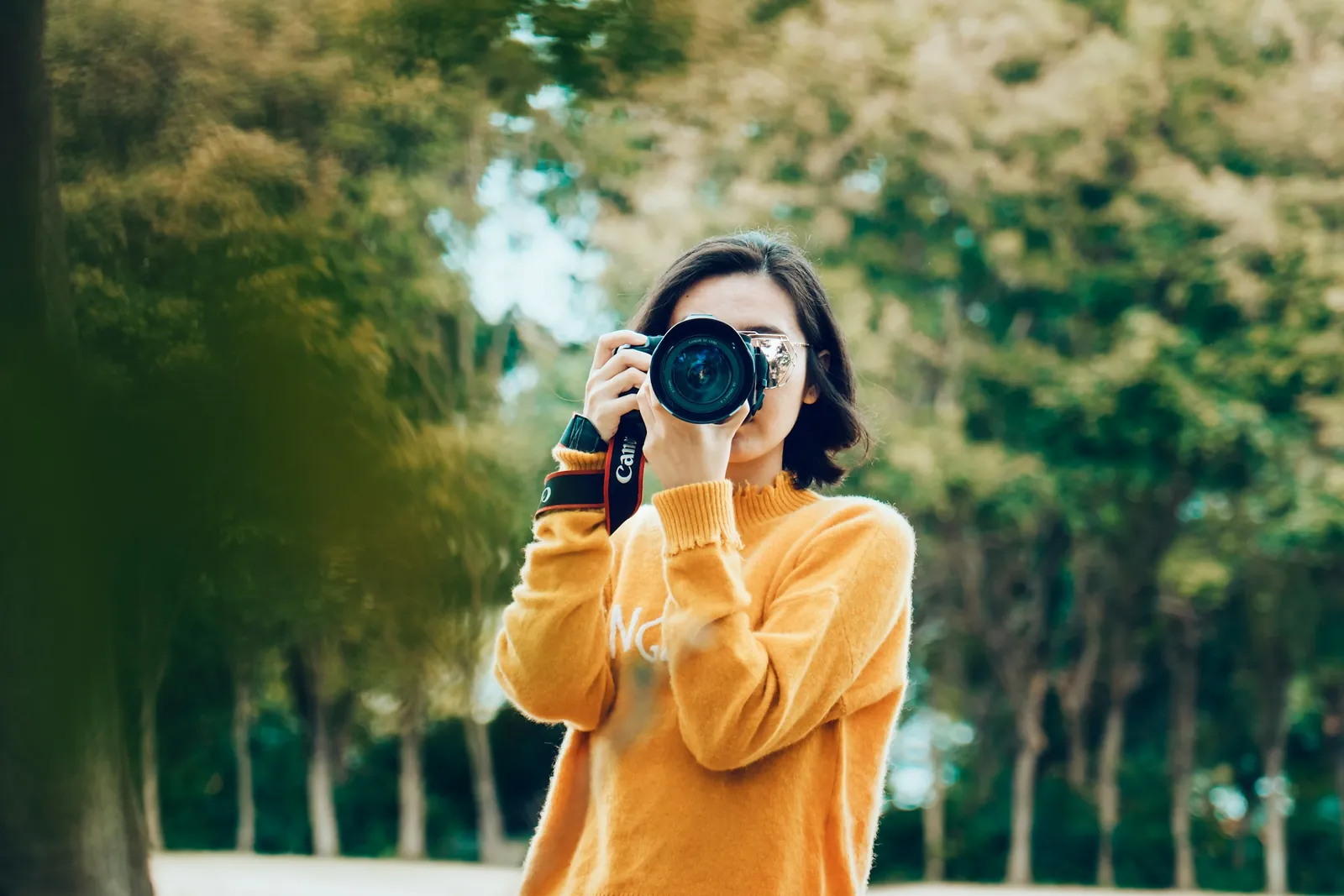 Photographer in a yellow sweater taking a picture outdoors among trees