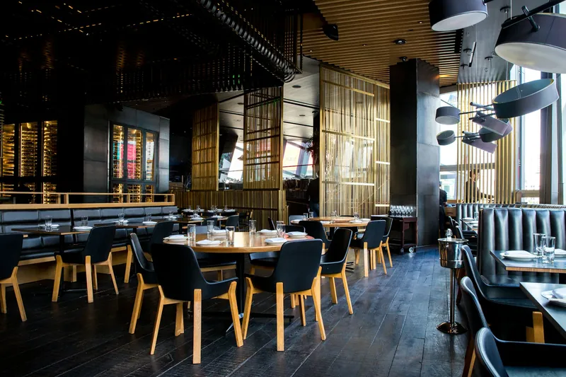 Dining room of a modern restaurant with dark wood tables, black chairs and warm pendant lights