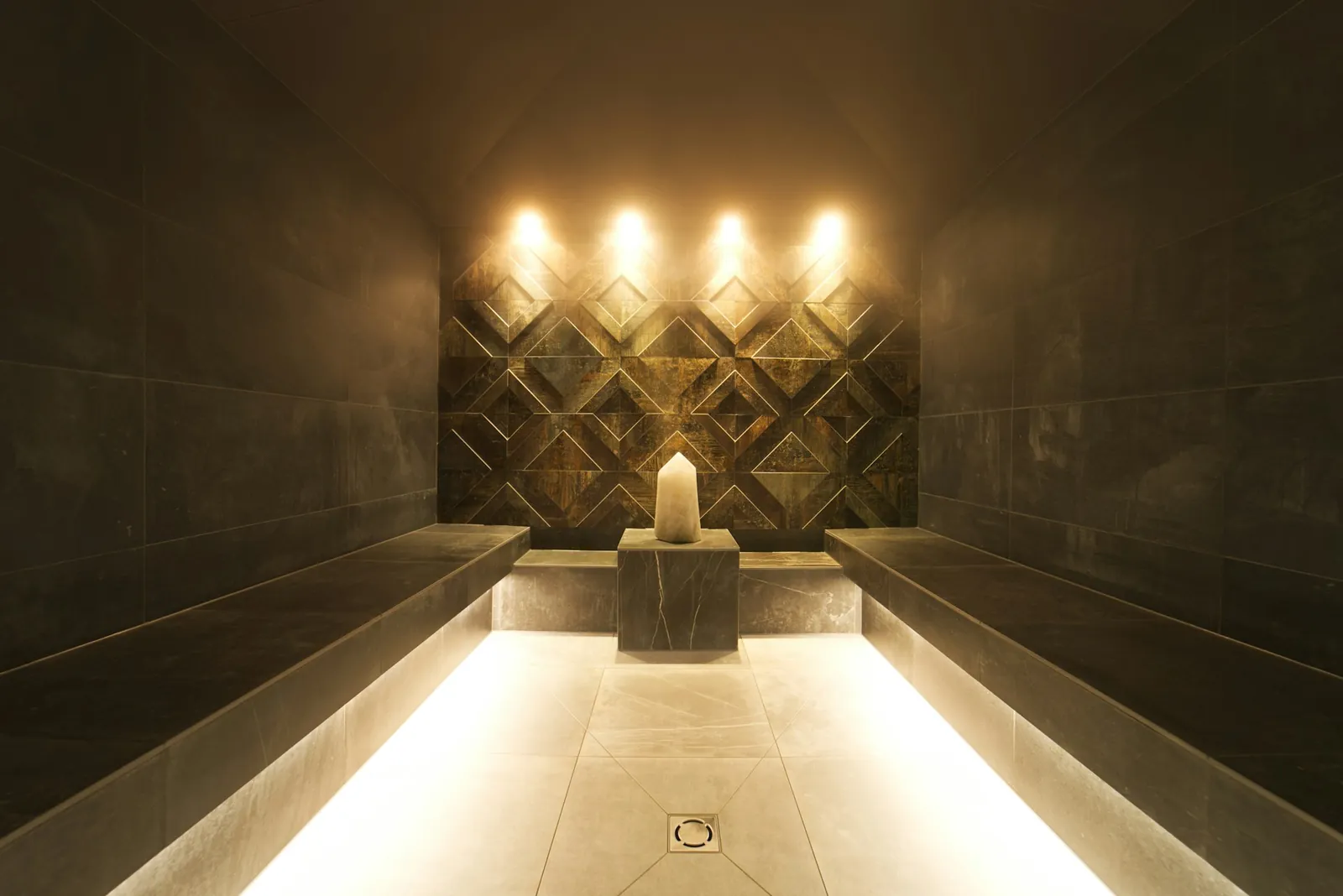 Softly lit spa steam room with stone benches and warm wall lights