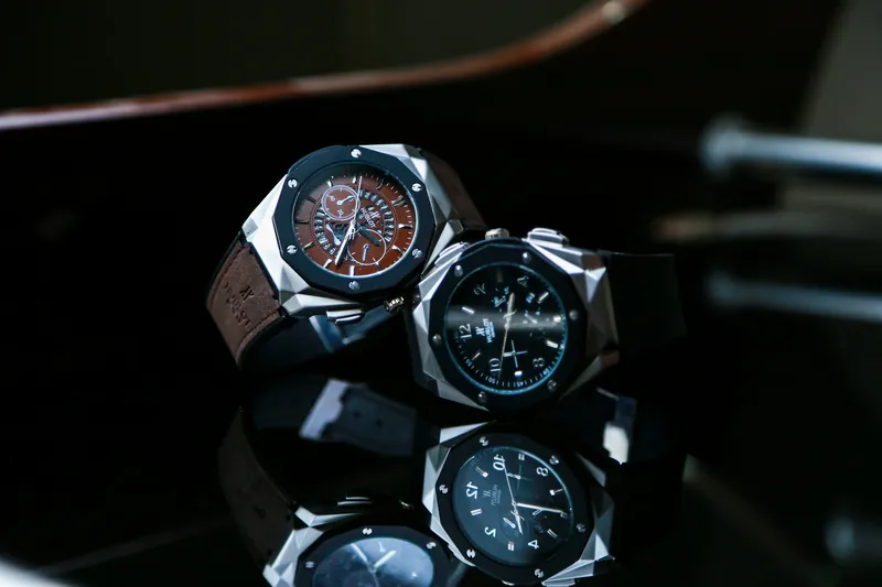 Three luxury wristwatches with steel cases on a dark reflective surface